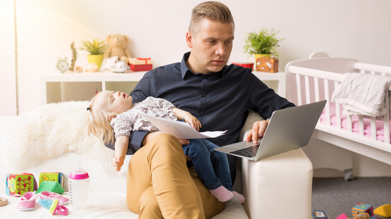 father caring for baby while working on computer