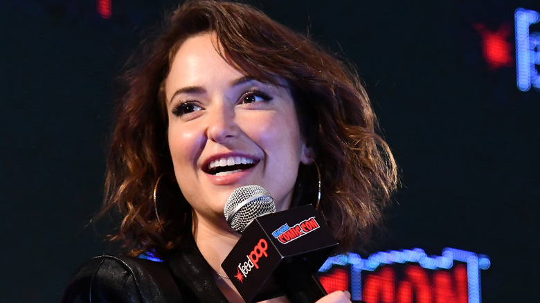 Milana Vayntrub smiling and holding a microphone