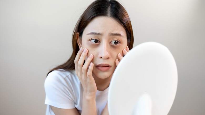 woman holding face looking in mirror