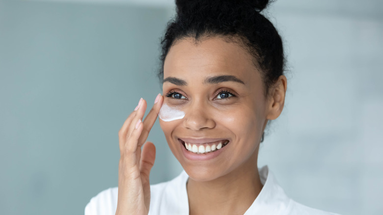 woman smiling putting on eye cream