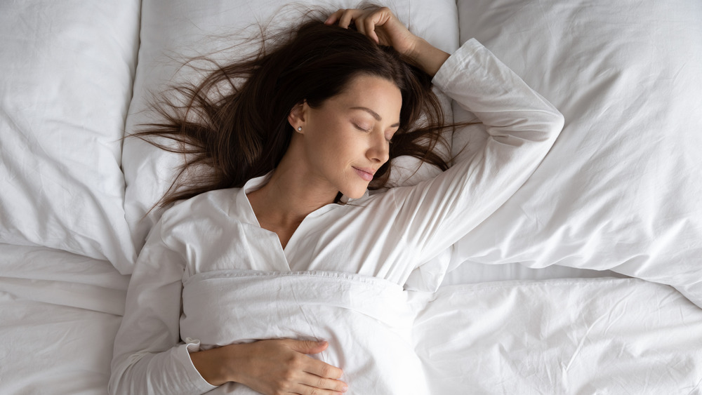 A woman happily sleeping white bedding 