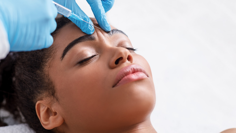 A Botox needle being placed into a woman's forehead 