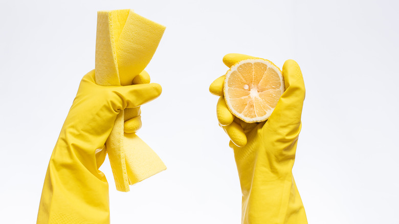 Hands with gloves holding a cleaning pad and a lemon