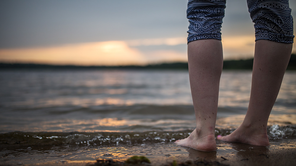 Person standing on shore as water laps feet