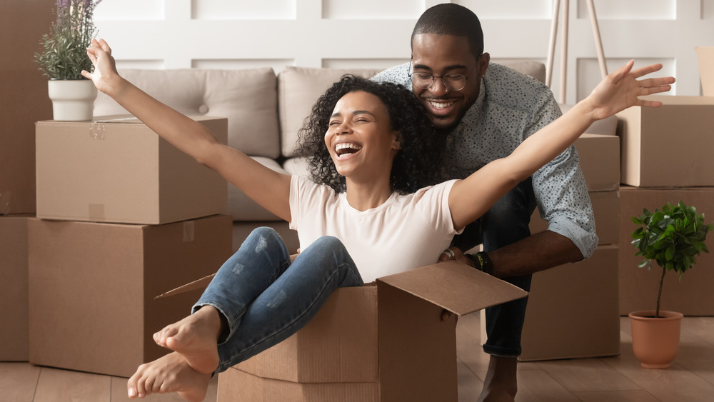 Woman smiling inside a cardboard box while smiling man stands behind her