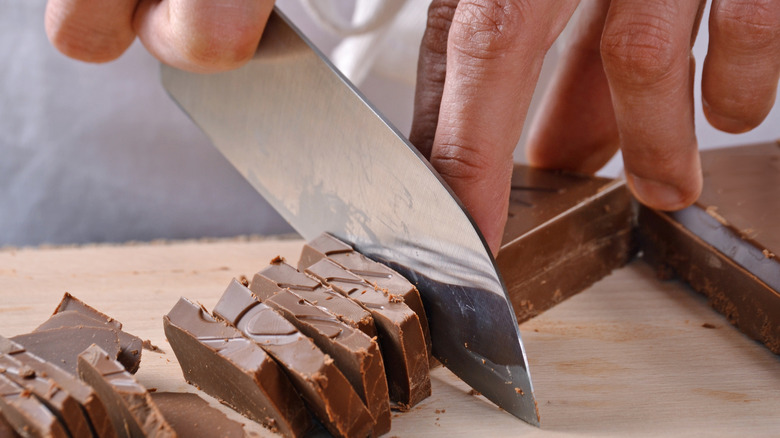 Hands cut chocolate on a wooden cutting board.