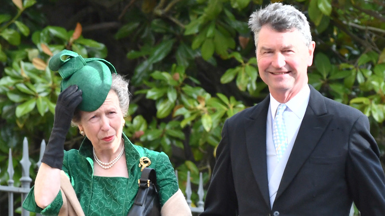 Princess Anne holding on to her hat and Timothy Laurence smiling