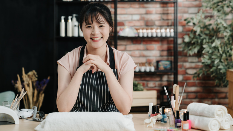 Japanese manicurist sitting at work station and smiling