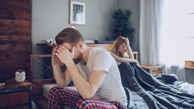 Man and woman sitting apart holding head in distress