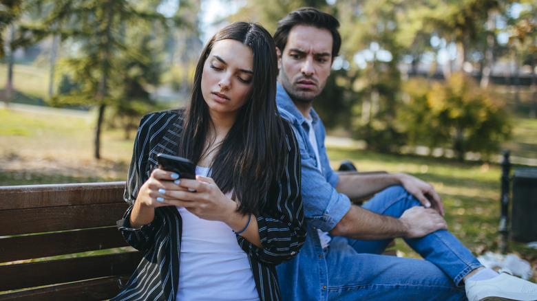 Man angrily looking over woman's shoulder as she texts