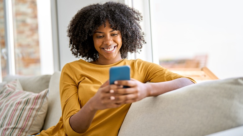 Woman smiling on couch looking at her phone