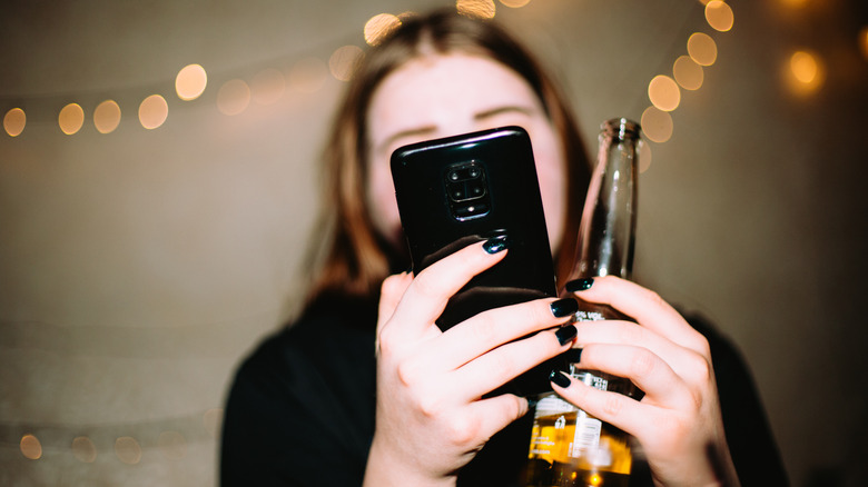 Woman holding her phone in one hand and a bottle of beer in the other