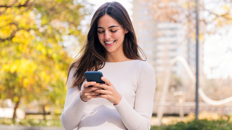 Woman standing outside while looking at phone and smiling