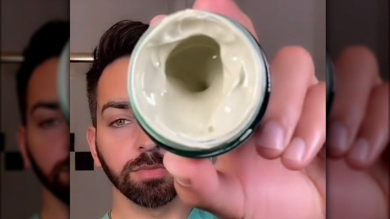 A man holding up a jar of moisturizer