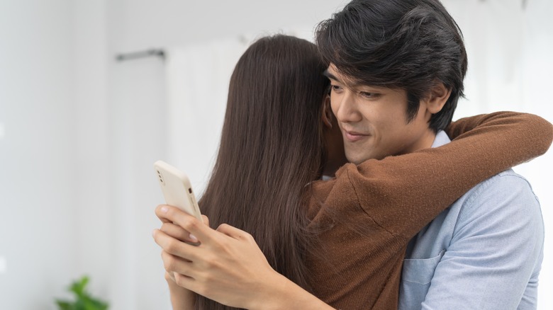 Man texting while hugging partner