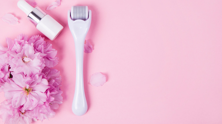 Derma roller and serum with pink flower decor on pink background