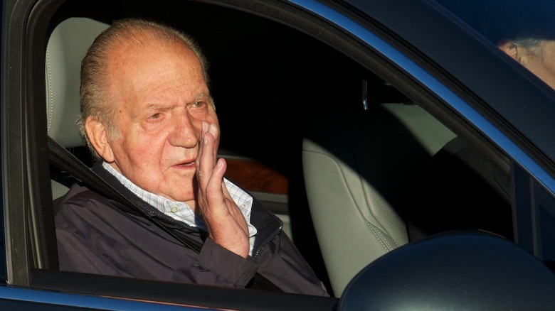 Former King Juan Carlos I seated in a car, waving to cameras