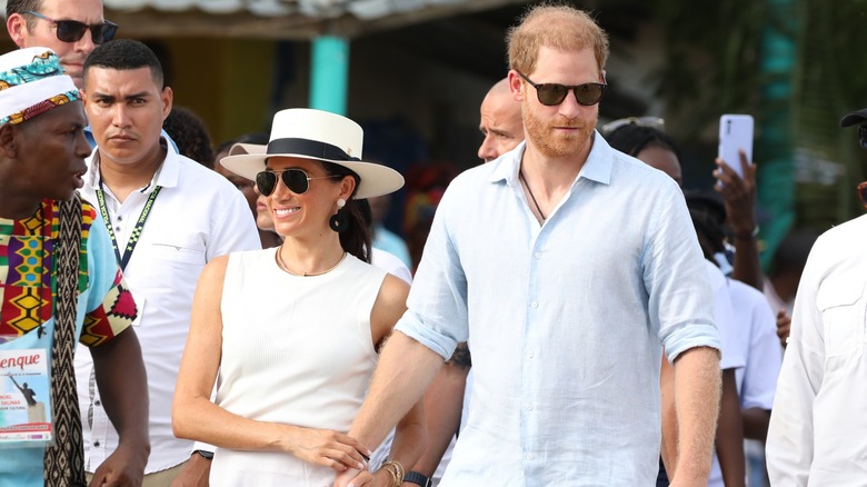 Meghan Markle smiling and holding Prince Harry's arm