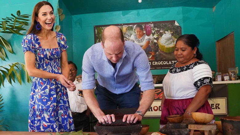 Prince William grinding cocoa nibs while Kate Middleton laughs and a Mayan woman looks on