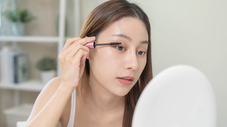 A woman applying mascara in a mirror 