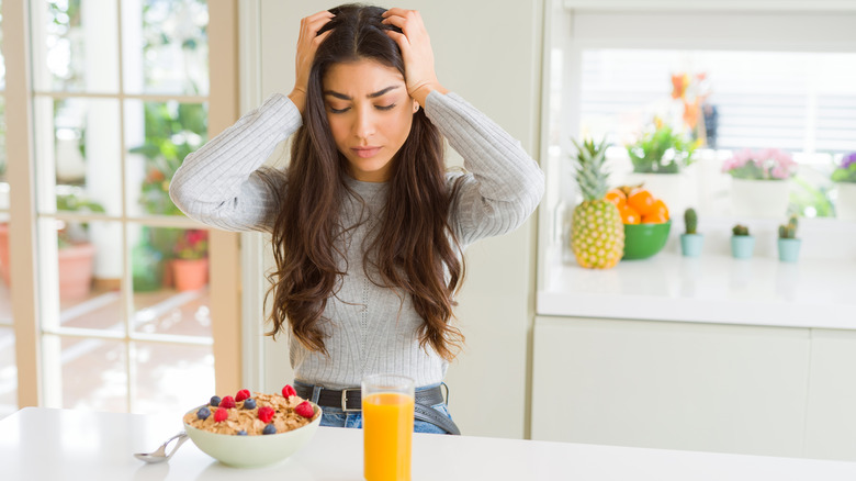 woman having juice for breakfast, with hands on head, due to headache 