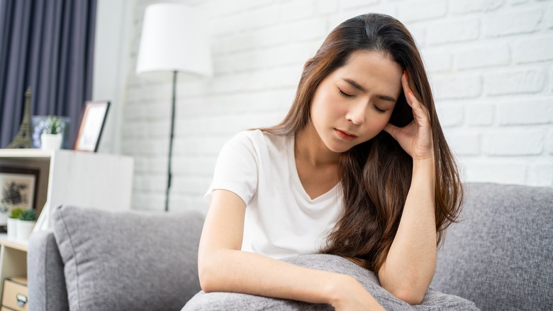 Woman with headache sitting on gray couch