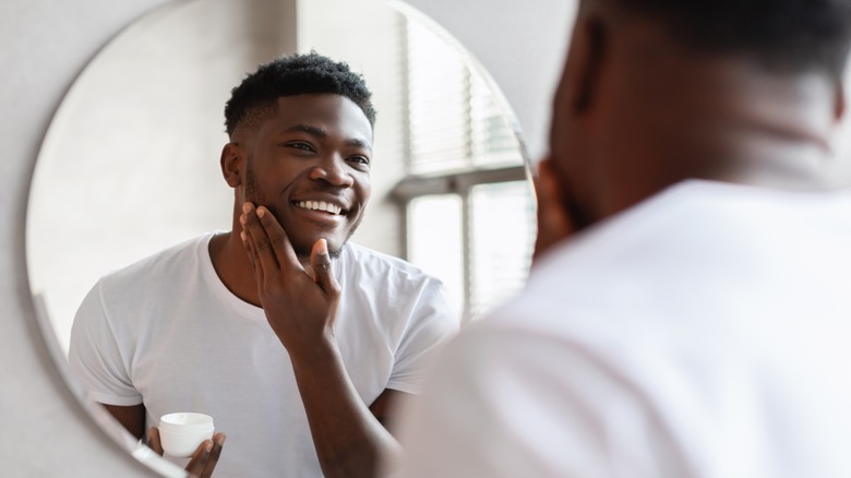 Man applying moisturizer in front of mirror