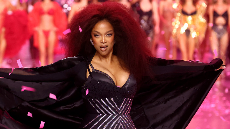 Tyra Banks on Victoria's Secret runway wearing black bustier with rhinestone geometric design and satin robe.