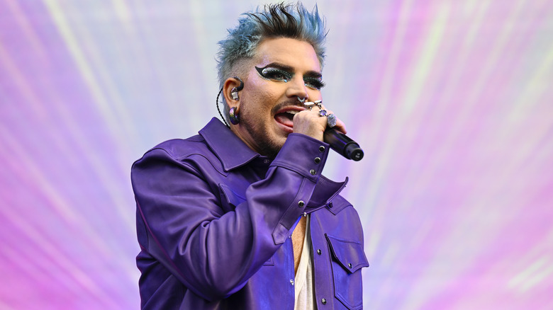 Adam Lambert performing onstage with blue hair and a purple jacket 