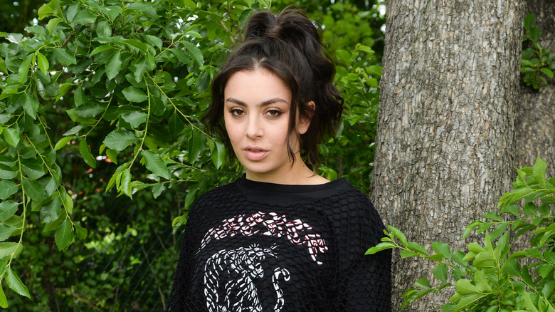 Charli XCX posing next to a tree