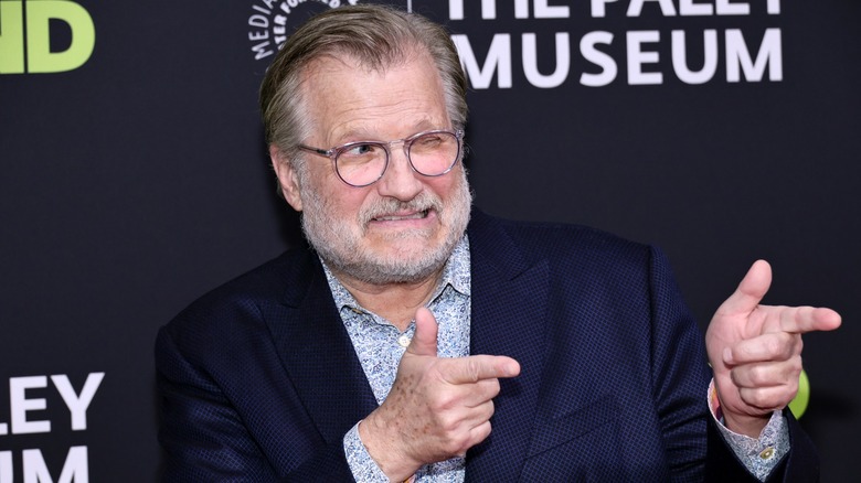 A bearded Drew Carey winking and pointing finger guns