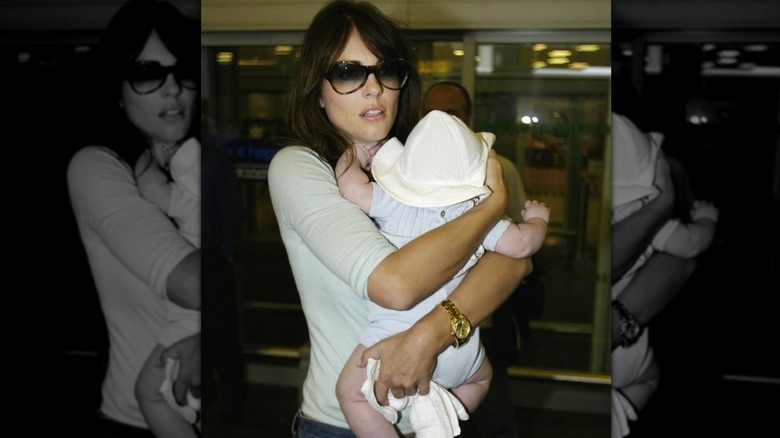 Elizabeth Hurley wearing sunglasses holding infant son wearing hat