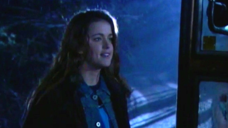 A trailer still from "Kaw" of Ashley Newbrough standing in the dark outside of an open school bus door