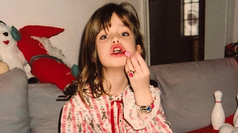 Ashley Newbrough at 9 years old, wearing holiday pajamas and putting on lipstick