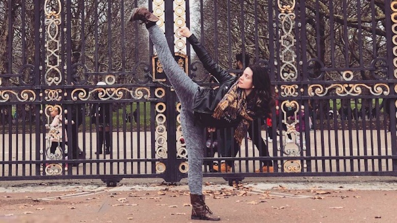 Lauren LaVera doing a martial arts high kick in front of the gates of Buckingham Palace