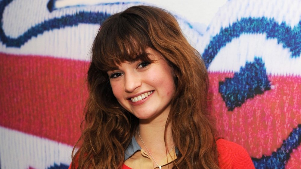 Lily James wearing a red sweater, smiling