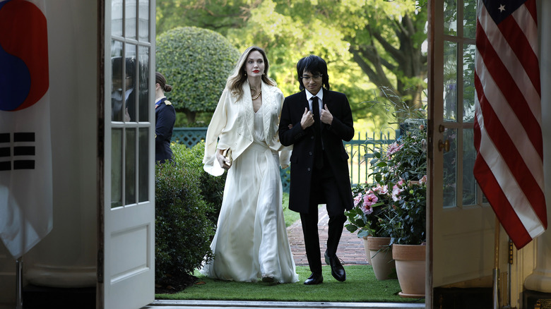 Angelina Jolie walking with Maddox Jolie-Pitt, each wearing formal attire 