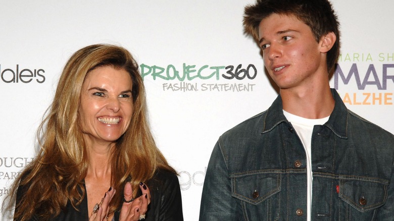 A clapping Maria Shriver and a teenage Patrick Schwarzenegger in front of a Project360 step-and-repeat