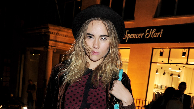 Suki Waterhouse standing outside in a hat