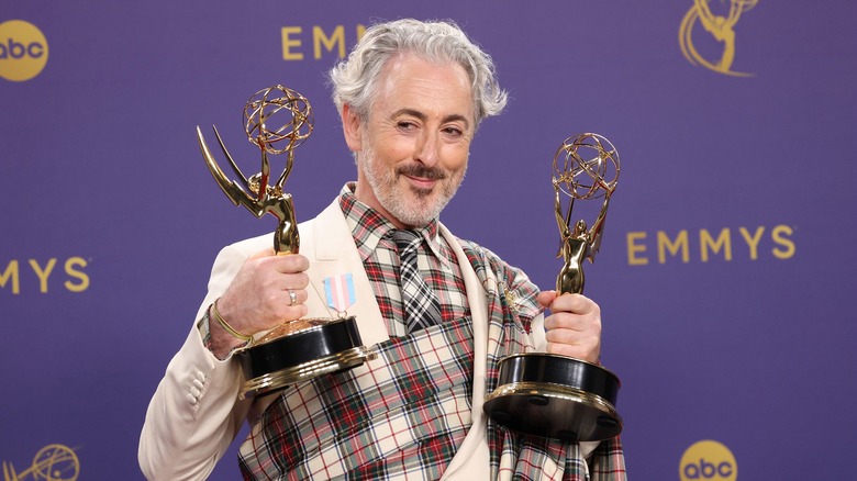 Alan Cumming holding two Emmy Awards on the Emmys red carpet