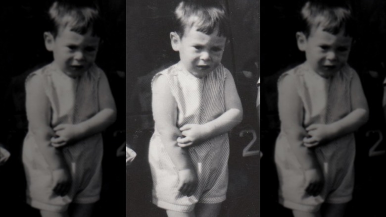 Alan Cumming as a child, holding his arm nervously