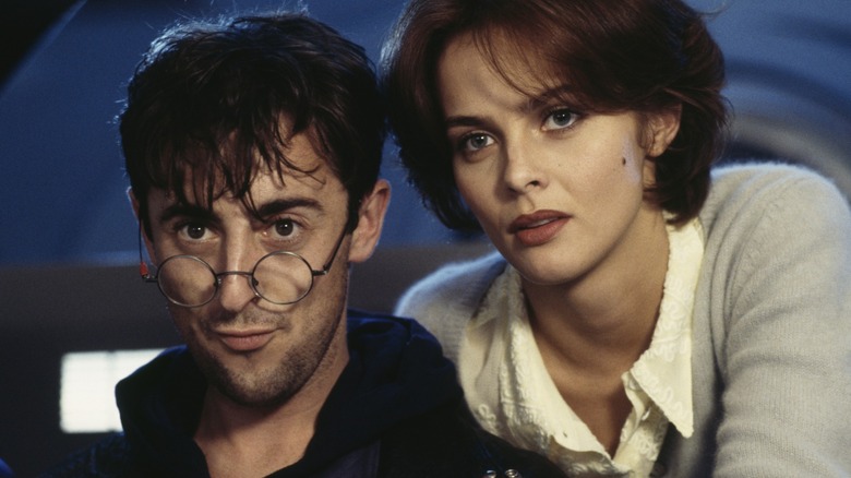 Alan Cumming with his glasses down on his nose, next to Izabella Scorupco, in GoldenEye