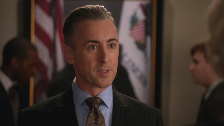 Alan Cumming as Eli Gold on The Good Wife, standing in front of a portrait