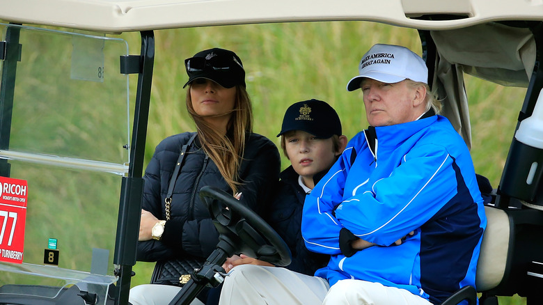 Melania, Barron, and Donald Trump sitting in golf cart