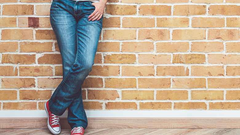 Woman wearing bootcut jeans posing by brick wall