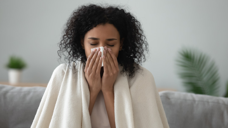 A woman sneezing into a tissue 