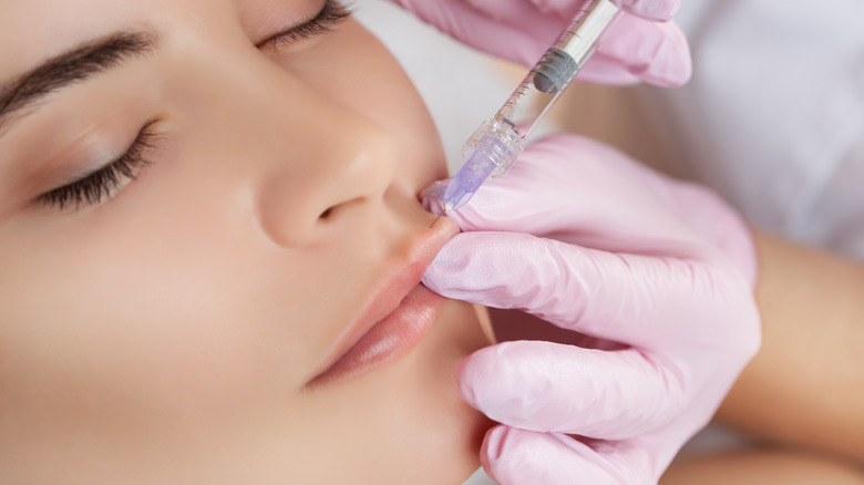 A gloved hand injecting filler into a woman's lips