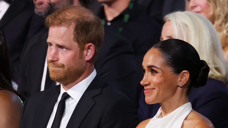 Prince Harry looking concerned while Meghan Markle smiles