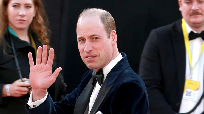 Prince William waving to a crowd with people in the background