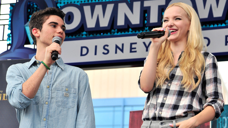 Cameron Boyce and Dove Cameron stand on stage together holding microphones